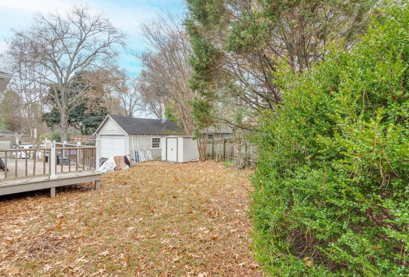 Fenced backyard with a detached garage, a wooden deck, and a storage unit