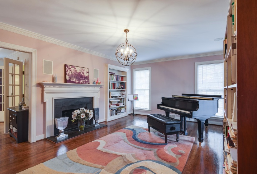 Living area with crown molding, a fireplace with raised hearth, dark wood-style floors, and a chandelier