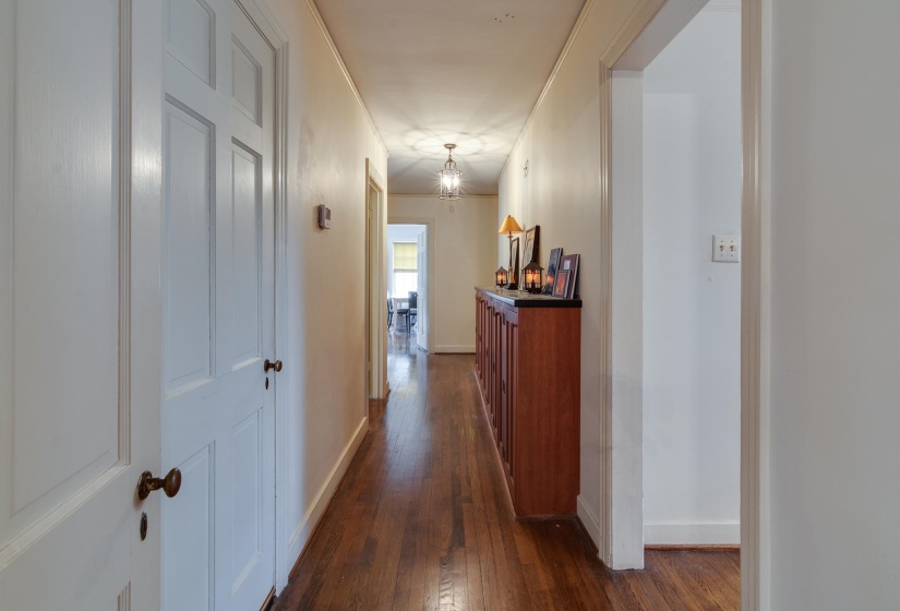 Hallway with dark wood-style flooring, ornamental molding, and a chandelier
