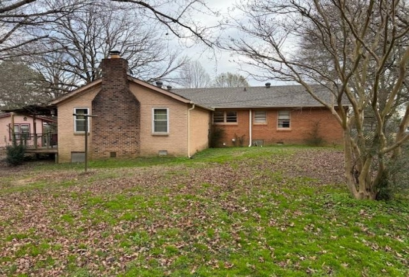 Back of property featuring crawl space, brick siding, a chimney, and a lawn