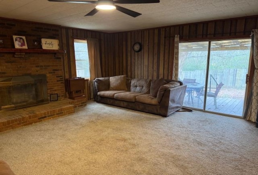 Carpeted living area with a fireplace, ceiling fan, and wooden walls