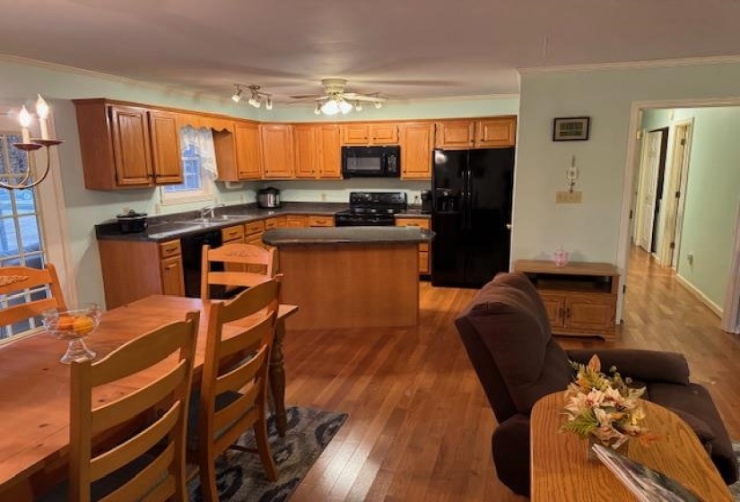 Kitchen with dark countertops, black appliances, ornamental molding, a kitchen island, and dark wood-type flooring