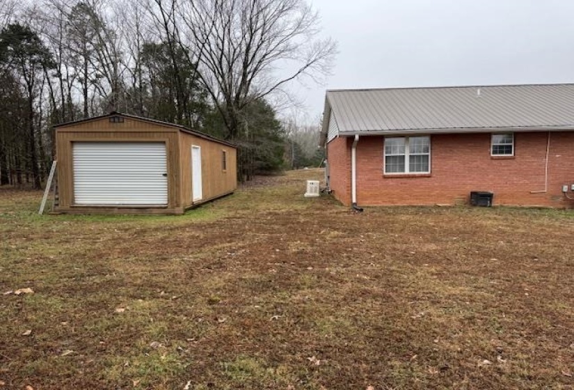 View of property exterior with a metal roof, brick siding, an outdoor structure, and a lawn
