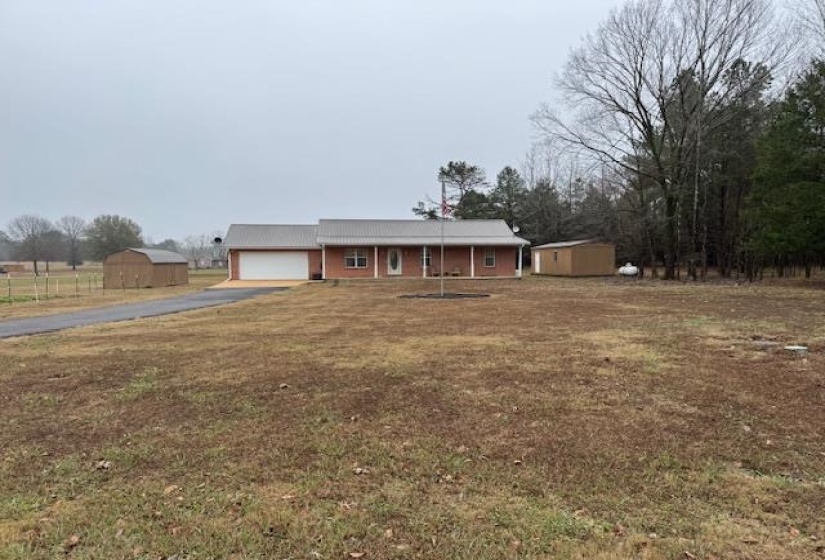 Single story home featuring asphalt driveway, a storage unit, a garage, and covered porch