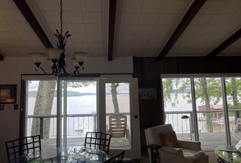 Dining space featuring beam ceiling, a water view, healthy amount of natural light, a chandelier, and wood walls
