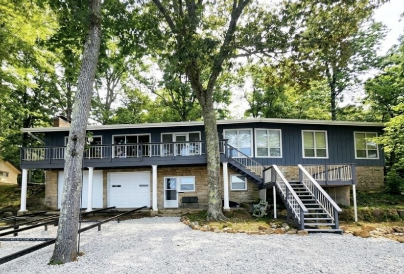 View of front facade with a garage, gravel driveway, a deck, stone siding, and a patio