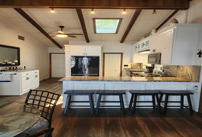 Kitchen featuring black appliances, dark stone countertops, white cabinetry, dark wood finished floors, and beam ceiling