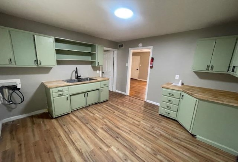 Kitchen with green cabinets, open shelves, and light wood-style flooring