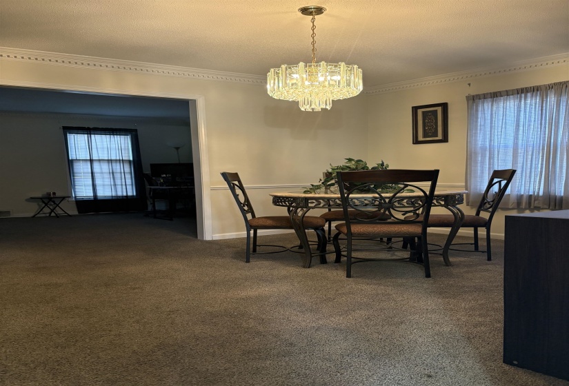 Carpeted dining area with a textured ceiling, a chandelier, and crown molding