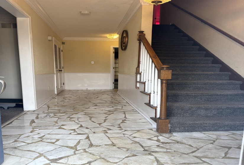 Stairs with ornamental molding, stone flooring, a wainscoted wall, and a textured ceiling