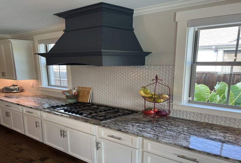 Kitchen featuring custom exhaust hood, tasteful backsplash, crown molding, white cabinetry, and stone counters