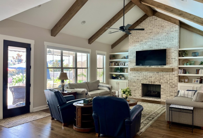 Living room featuring dark wood-style flooring, high vaulted ceiling, a fireplace, beam ceiling, and ceiling fan