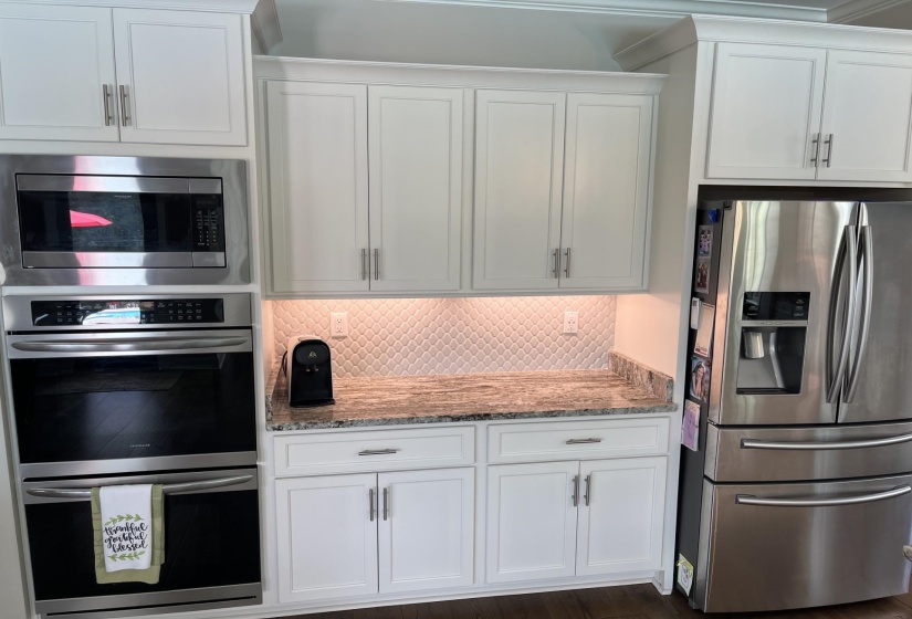 Kitchen featuring stainless steel appliances, decorative backsplash, white cabinetry, and light stone countertops