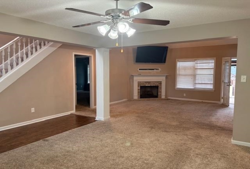 Unfurnished living room featuring stairway, a brick fireplace, carpet, a ceiling fan, and a textured ceiling