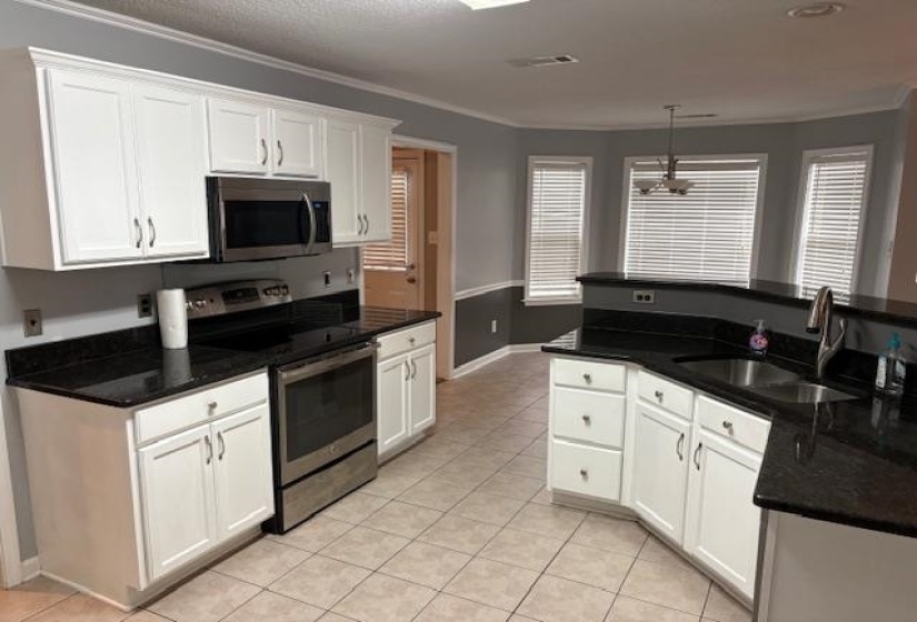 Kitchen featuring stainless steel appliances, white cabinets, light tile patterned floors, dark stone counters, and ornamental molding