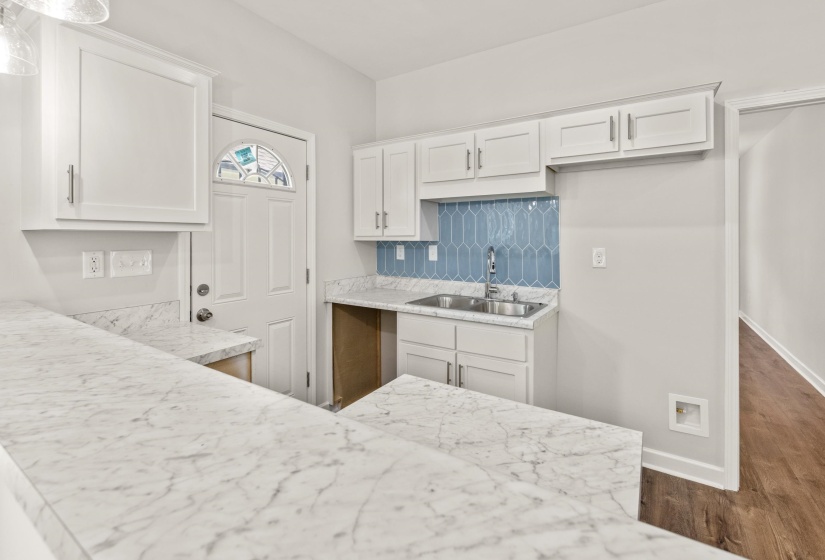 Kitchen with white cabinets, decorative backsplash, light stone countertops, and dark wood-type flooring
