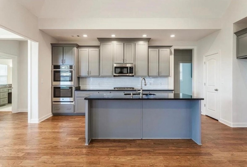 Kitchen featuring gray cabinets, a center island with sink, stainless steel appliances, light wood-type flooring, and recessed lighting