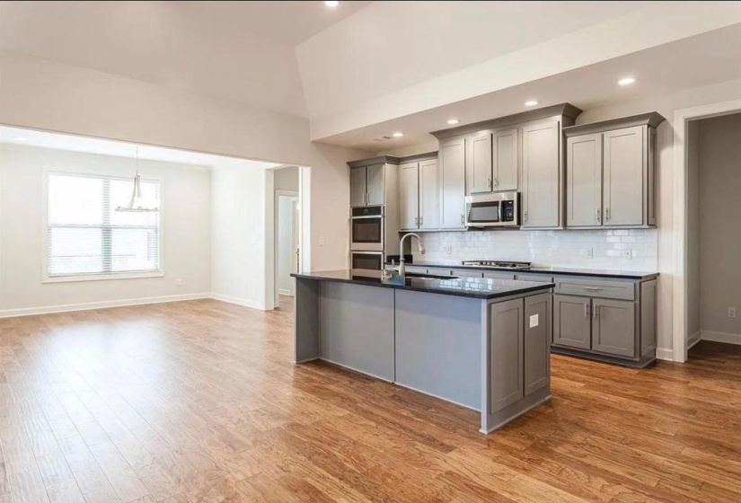 Kitchen with gray cabinetry, a center island with sink, appliances with stainless steel finishes, backsplash, and light wood-style floors