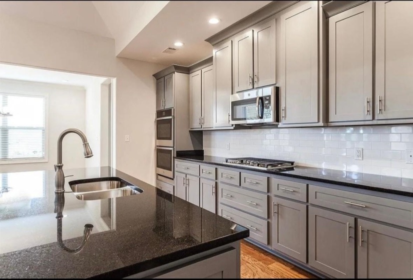 Kitchen with gray cabinetry, dark stone counters, tasteful backsplash, appliances with stainless steel finishes, and light wood-type flooring