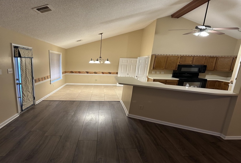 Kitchen with beam ceiling, kitchen peninsula, wood-type flooring, black appliances, and ceiling fan with notable chandelier