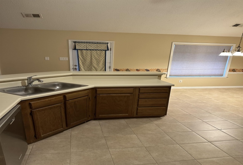 Kitchen featuring dishwasher, sink, hanging light fixtures, a textured ceiling, and light tile patterned floors