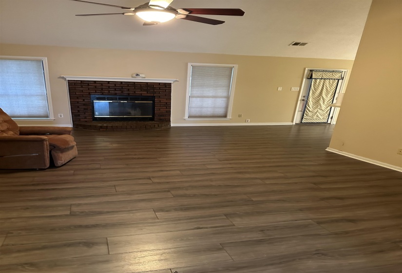 Unfurnished living room with a brick fireplace, ceiling fan, plenty of natural light, and dark hardwood / wood-style flooring