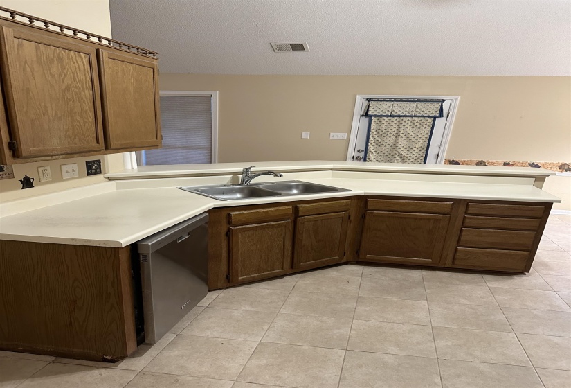 Kitchen with a textured ceiling, light tile patterned floors, sink, dishwasher, and kitchen peninsula