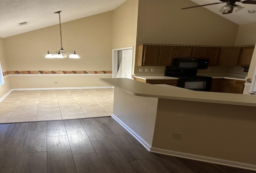 Kitchen with high vaulted ceiling, light hardwood / wood-style flooring, black appliances, and decorative light fixtures
