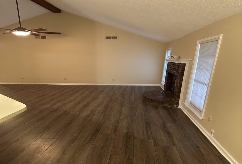 Unfurnished living room with beamed ceiling, dark hardwood / wood-style floors, a wealth of natural light, and a brick fireplace