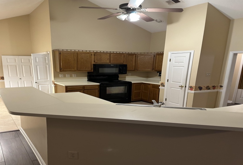 Kitchen with kitchen peninsula, ceiling fan, black appliances, light hardwood / wood-style flooring, and high vaulted ceiling