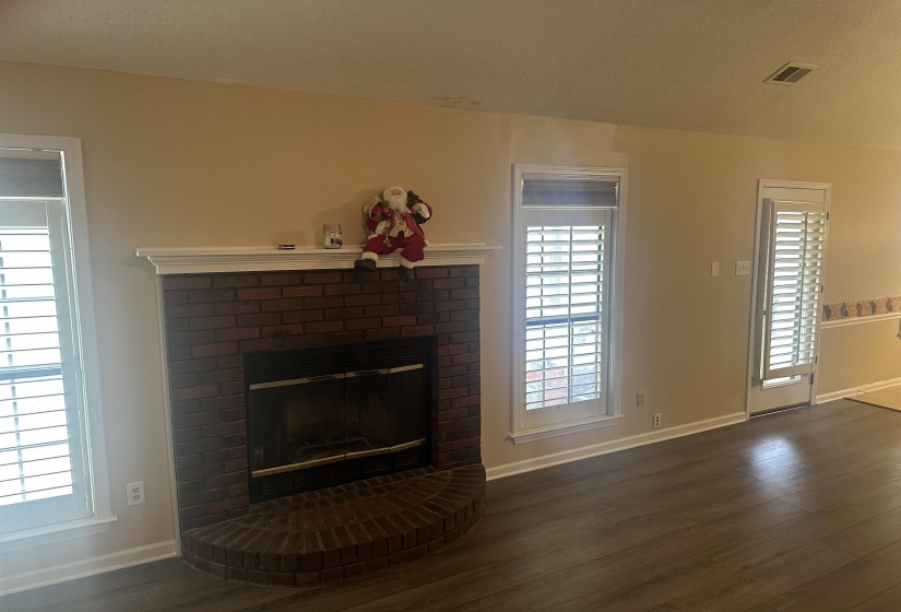 Unfurnished living room featuring dark wood-type flooring and a brick fireplace