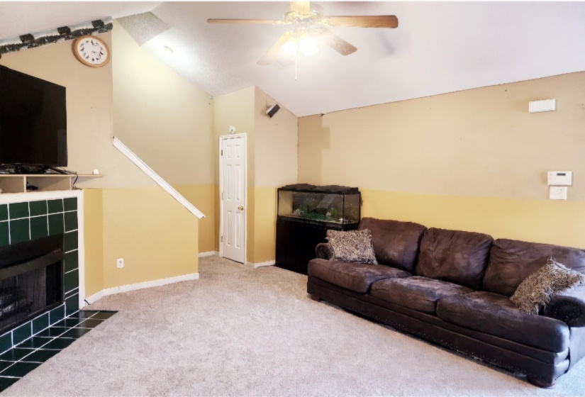Carpeted living room with a fireplace, vaulted ceiling, and ceiling fan