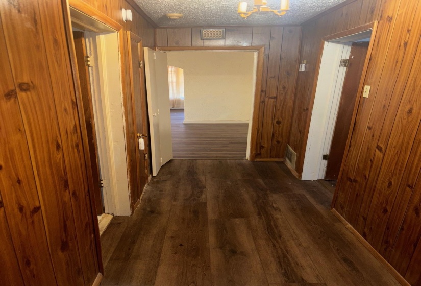 Corridor with a textured ceiling, wood walls, dark wood-style flooring, and a chandelier