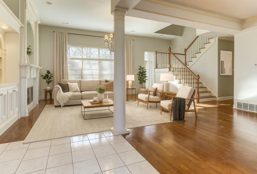 Living area with light wood finished floors, ornate columns, a glass covered fireplace, a chandelier, and stairs