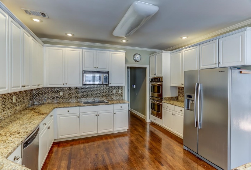 Kitchen with light stone countertops, dark hardwood / wood-style flooring, backsplash, stainless steel appliances, and white cabinetry