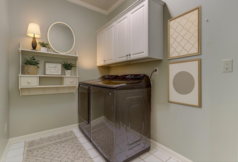 Laundry room with crown molding, cabinet space, washing machine and dryer, and light tile patterned floors