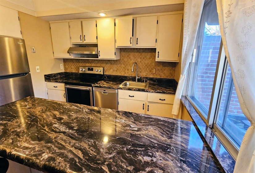 Kitchen with appliances with stainless steel finishes, dark stone countertops, backsplash, and extractor fan