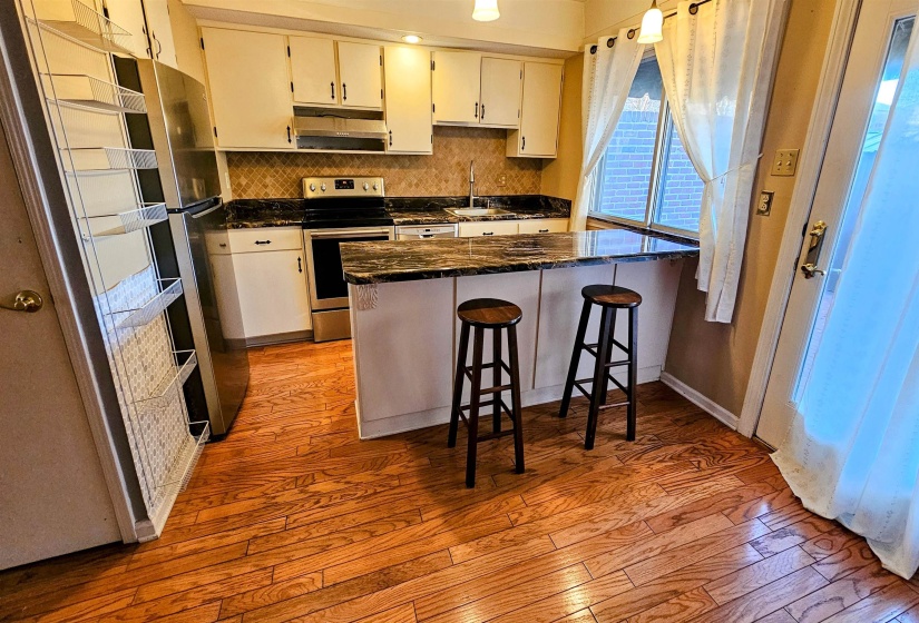 Kitchen featuring appliances with stainless steel finishes, a kitchen breakfast bar, light wood-style flooring, tasteful backsplash, and dark stone countertops
