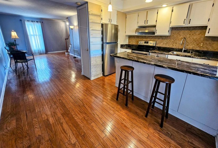 Kitchen with decorative backsplash, dark stone counters, stainless steel appliances, dark wood finished floors, and a breakfast bar