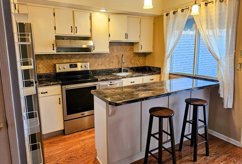 Kitchen with appliances with stainless steel finishes, decorative backsplash, a kitchen bar, light wood finished floors, and under cabinet range hood