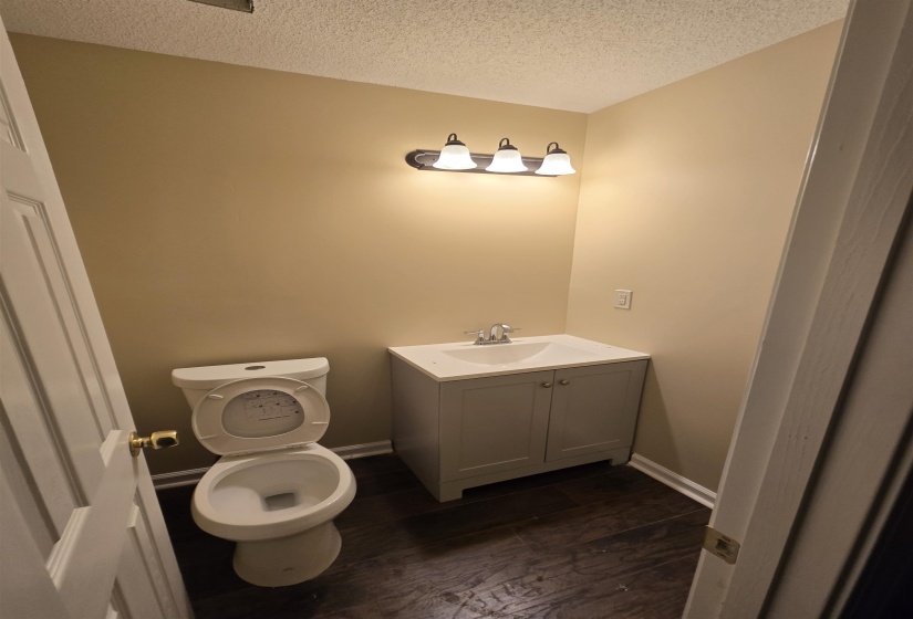 Bathroom with wood-type flooring, toilet, vanity, and a textured ceiling