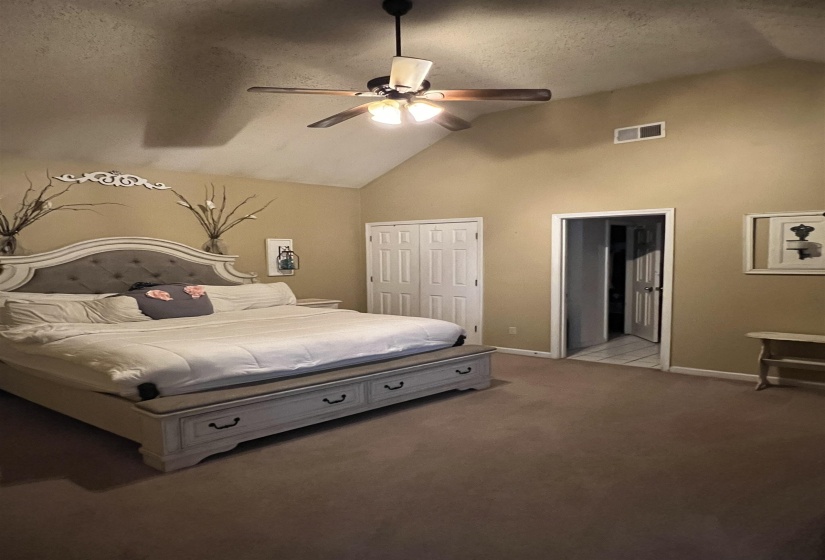 Bedroom with vaulted ceiling, a textured ceiling, light carpet, ceiling fan, and a closet