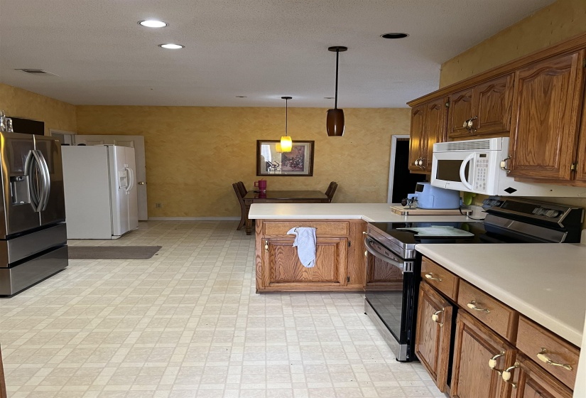 Kitchen with range with electric stovetop, brown cabinetry, stainless steel fridge, light countertops, and a peninsula
