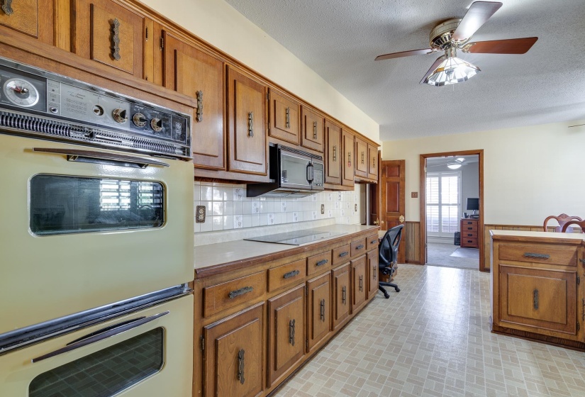 Kitchen with black appliances, brown cabinets, a wainscoted wall, light countertops, and a textured ceiling