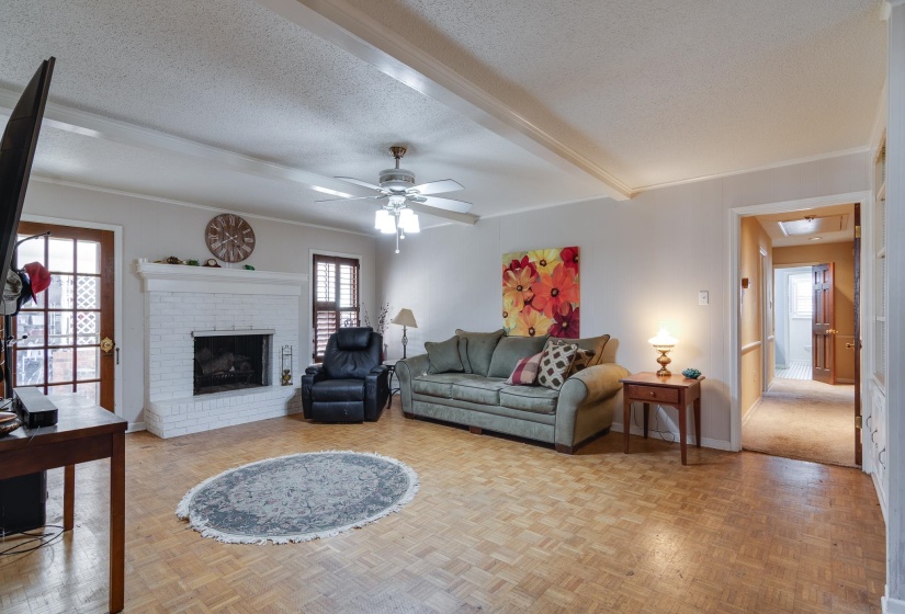 Living room featuring beamed ceiling, a textured ceiling, a fireplace, and a ceiling fan