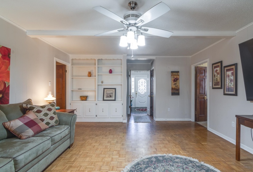 Living room with ornamental molding, ceiling fan, and built in features