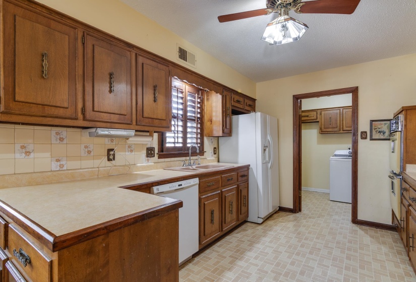 Kitchen with brown cabinetry, white appliances, light countertops, washer / clothes dryer, and brick patterned flooring