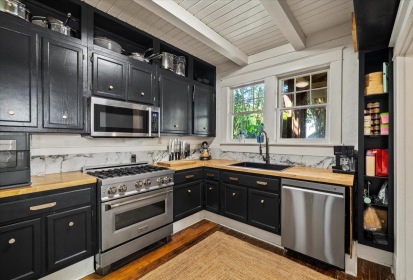Kitchen featuring dark cabinets, butcher block countertops, stainless steel appliances, dark wood-style flooring, and a wood ceiling with exposed beams