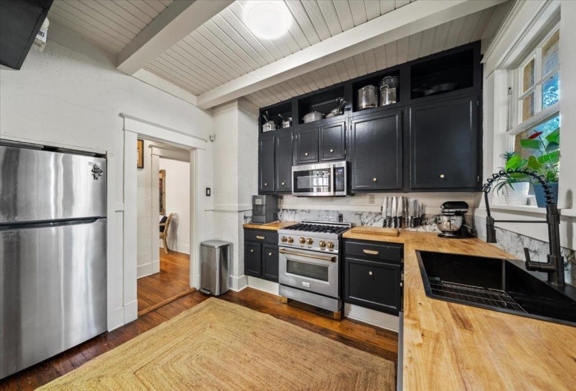 Kitchen featuring dark cabinets, butcher block counters, appliances with stainless steel finishes, dark wood-type flooring, and a wood ceiling with exposed beams