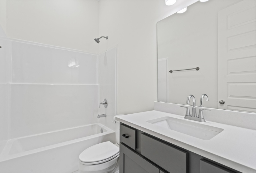 Bathroom featuring a white integrated sink, gray cabinet vanity with black hardware, white tub-shower combination, polished chrome fixtures, and a large wall-mounted mirror